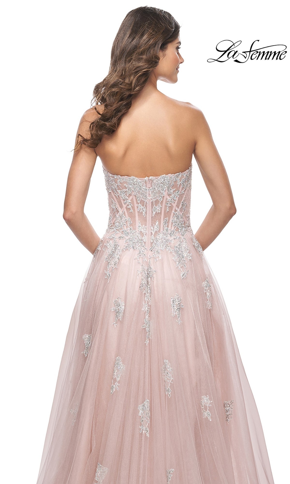 A woman is seen from the back wearing the La Femme Strapless Long A-Line Prom Dress 32111 with pink tulle, silver embroidery, a fitted corset-style bodice, embroidered lace appliques, and a flowing skirt.